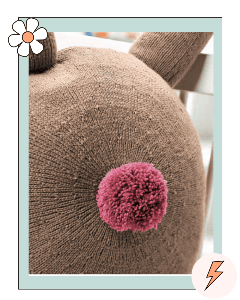 Knitted rabbit cushion back view showing pompom tail, free bunny cushion knitting pattern in DK yarn jane burns