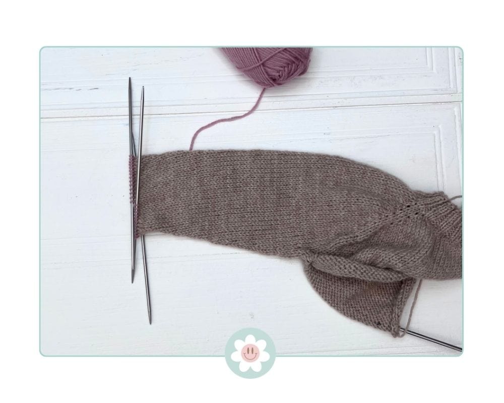 Image shows, one round of contrasting colour ahead of ribbing  on a top-down children's cardigan, cuff stitches on needle ready for ribbing how-to-knit-a-top-down-cardigan-for-kids