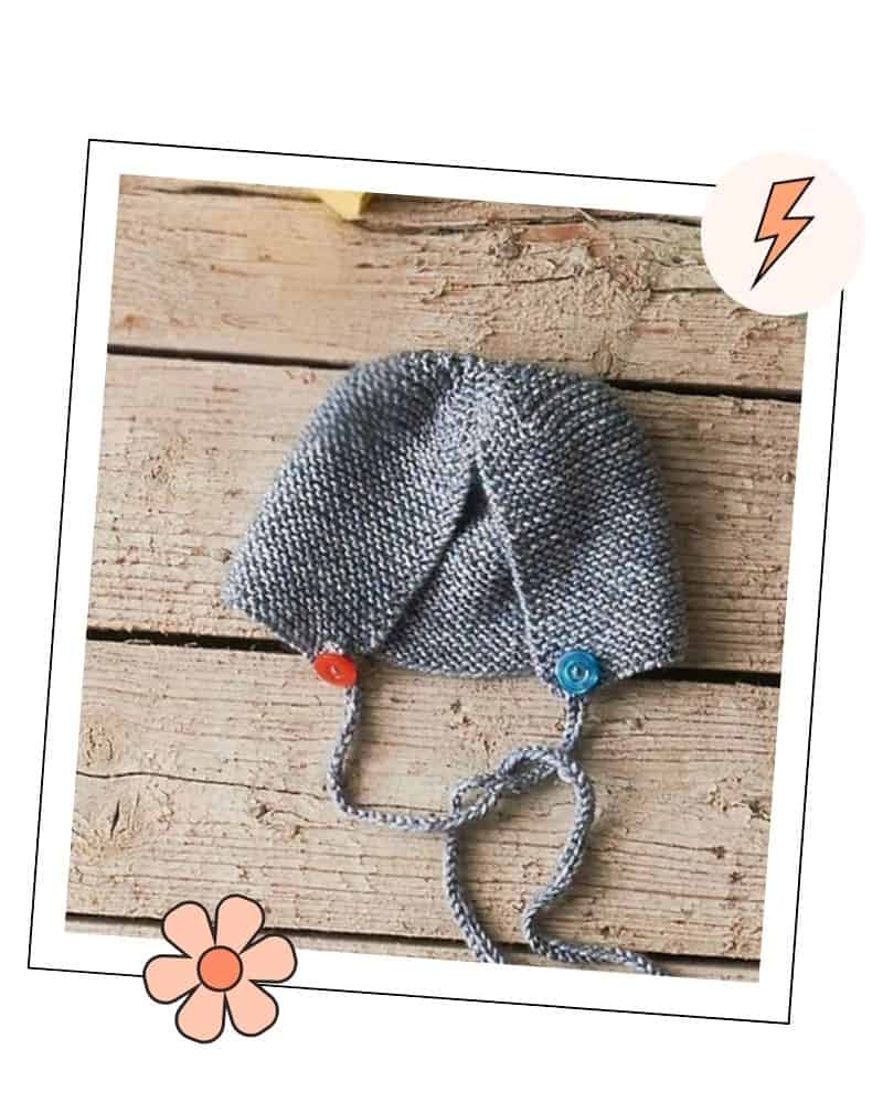 Grey garter stitch baby bonnet with knitted ties, laid flat in a decorative photo frame